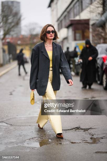 Guest wears black sunglasses, silver earrings, a silver chain necklace, a black oversized blazer jacket, a yellow ribbed wool shoulder-off t-shirt, a...