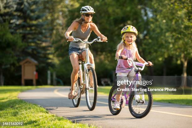 a young girl rides bikes with her mom in a park - bicycle daughter stock-fotos und bilder