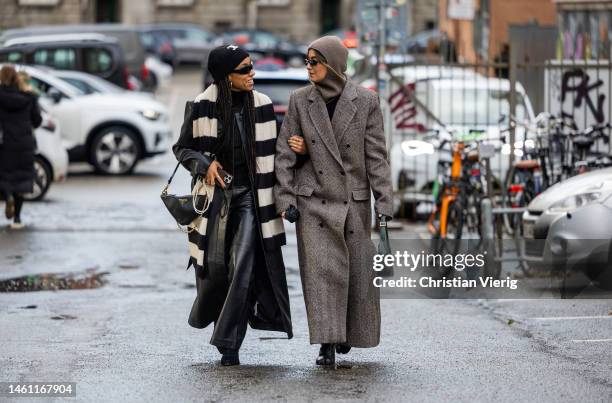 Amaka Hamelijnck wears black white striped scarf, Prada bag, Celine beanie, black coat, leather pants & Benthe Liem wears brown balaclava, grey...