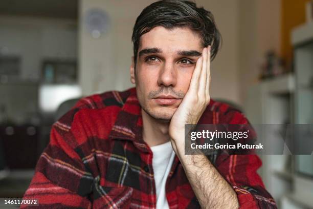 trauriger, unglücklicher, gutaussehender mann, der auf dem sofa sitzt und sich die stirn hält, während er kopfschmerzen hat - bedauern stock-fotos und bilder