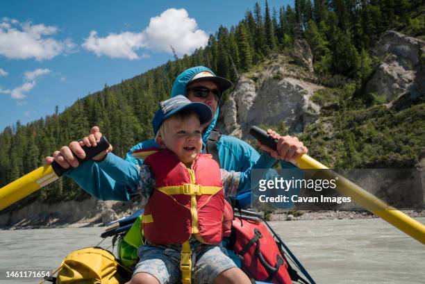 a father and son row a raft down a large river in the mountains - kids at river photos et images de collection
