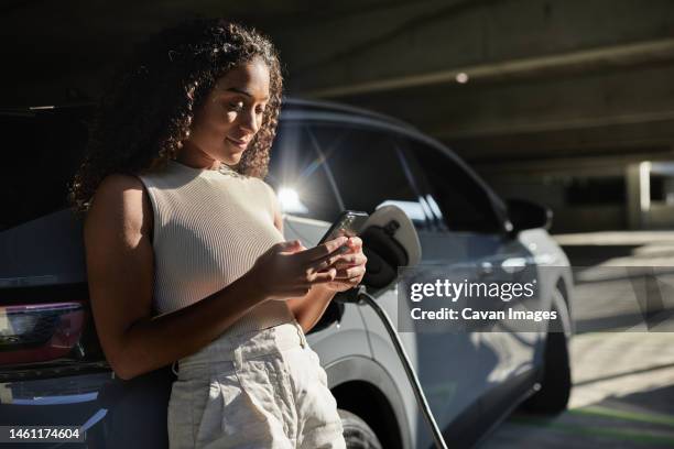 woman using smart phone by electric car at parking garage - tesla interior stock pictures, royalty-free photos & images