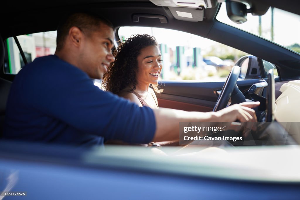 Smiling couple using GPS while sitting in electric car