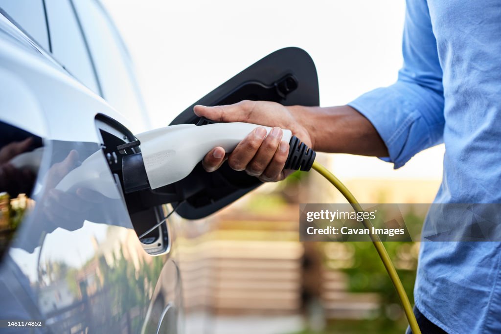 Midsection of man plugging in cable while charging electric car