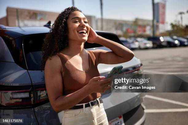 woman with smart phone laughing in parking lot on sunny day - phone leaning stock pictures, royalty-free photos & images