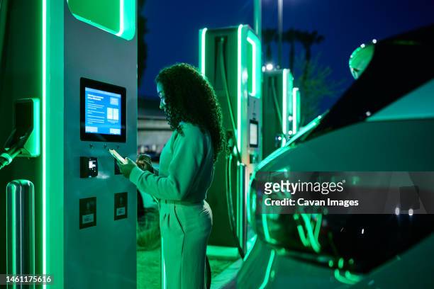 woman standing at charging station during night - electric vehicle charging station stock pictures, royalty-free photos & images