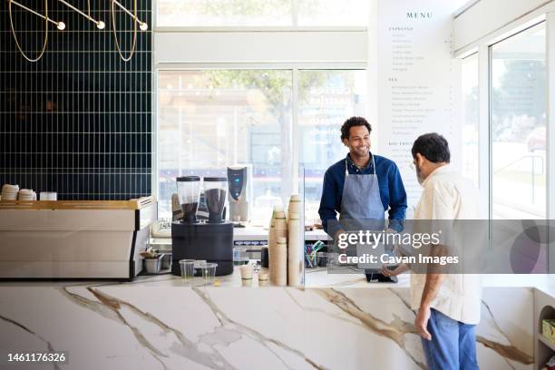 mature customer doing contactless payment at checkout counter in cafe - kassierer stock-fotos und bilder