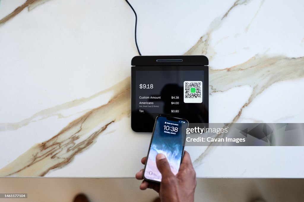Cropped hand of customer taping smart phone on marble counter