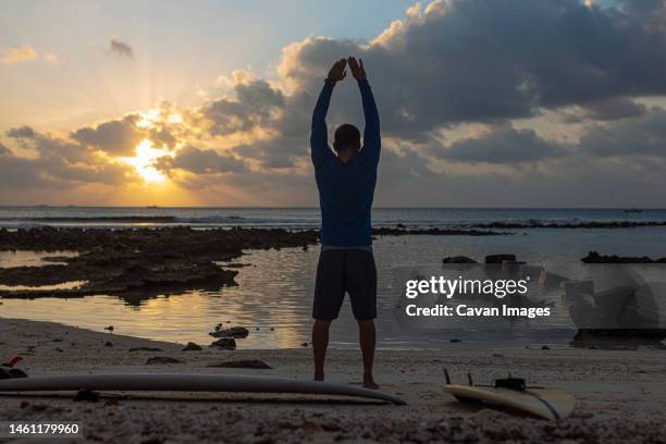 male surfer practising yoga at the beach - thulusdhoo stock pictures, royalty-free photos & images