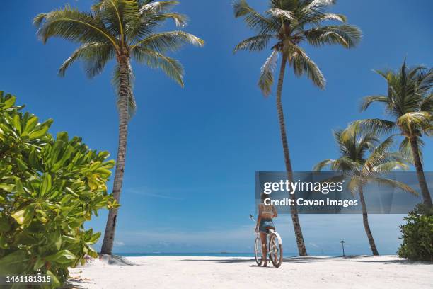 woman riding bicycle on the beach - thulusdhoo stock pictures, royalty-free photos & images