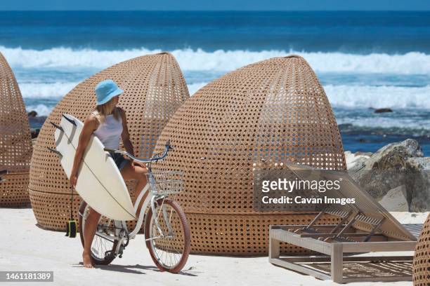 woman with surfboard riding bicycle on the beach - thulusdhoo stock pictures, royalty-free photos & images