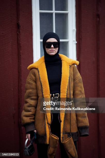 Guest wears a black wool hoodie or balaclava, black squared sunglasses, black shiny leather belts, a yellow suede with sheep interior oversized coat,...