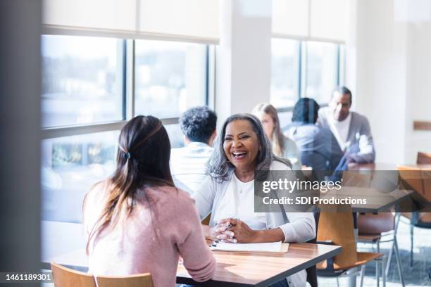 senior woman smiles while assisting unrecognizable woman at job fair - job fair stock pictures, royalty-free photos & images