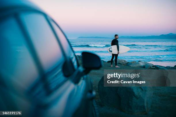 a middle aged surfer looks out towards the beach at blue hour - surfing stock pictures, royalty-free photos & images