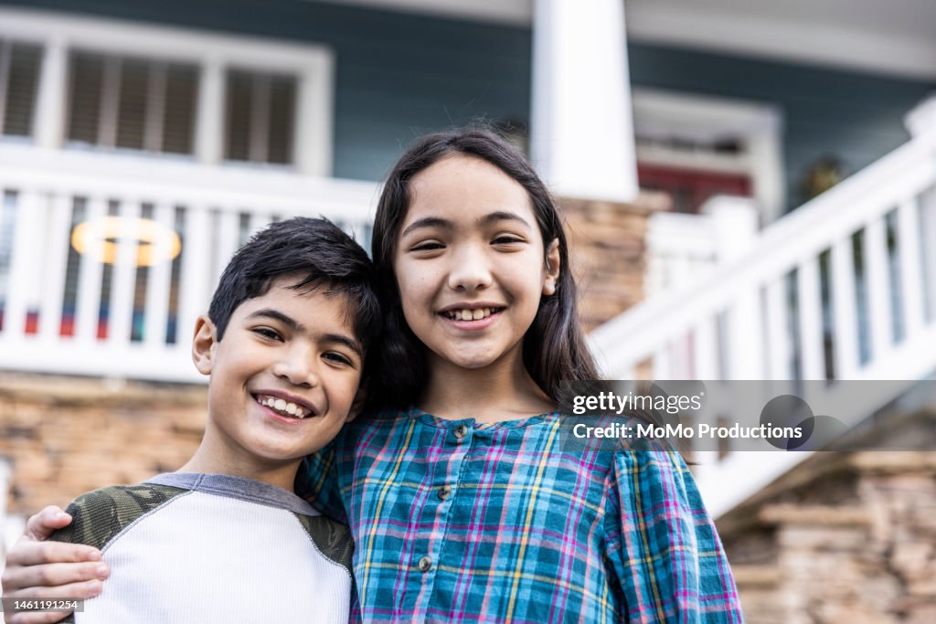 Portrait of brother and sister in front of urban home