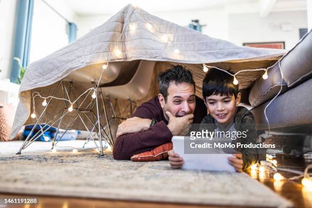 father and son watching a movie on digital tablet in homemade fort - kids fort imagens e fotografias de stock