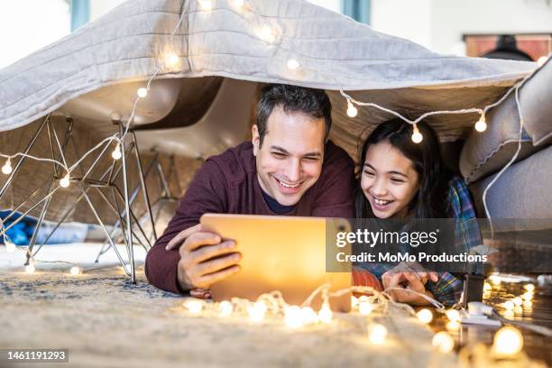 father and daughter watching a movie on digital tablet in homemade fort - streaming service stock pictures, royalty-free photos & images