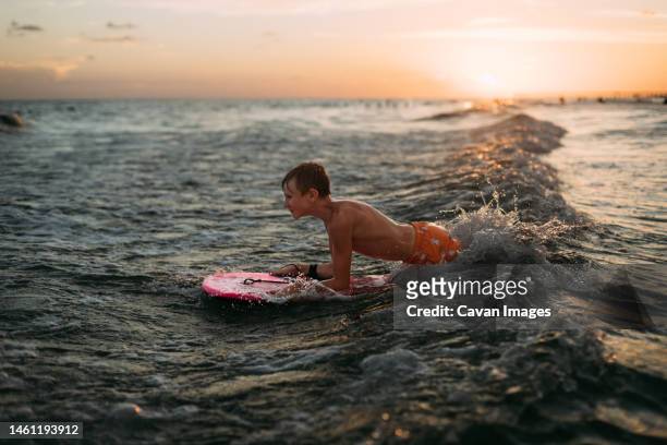 young boy wake boarding in ocean waves at sunset - extreem weer stock pictures, royalty-free photos & images