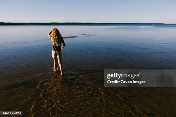 girl walks in shallow water on beach with blue sky and sunshine - lake superior stock-fotos und bilder