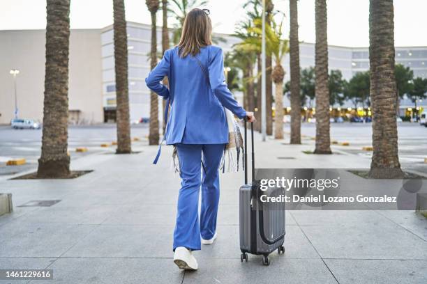 back view of stylish woman walking through a tropical airport walkway carrying travel suitcase - woman full body behind stock-fotos und bilder