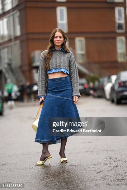 Guest wears gold earrings, a blue and white striped print pattern cropped shirt, a dark gray braided wool cropped pullover , a navy blue denim...