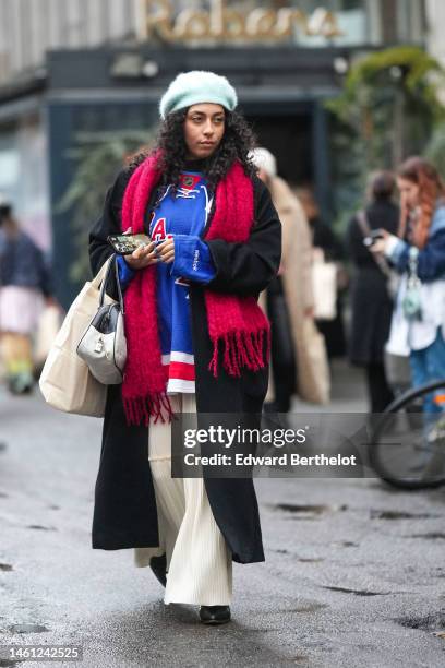 Guest wears a pale blue wool beret, a royal blue with red and white print pattern oversized t-shirt, a red wool fringed scarf, a black long wool...