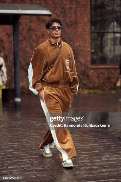 Guest wearing a brown sweat suit with blue and white stripes and orange sunglasses with a blue frame outside Stamm during the Copenhagen Fashion Week...