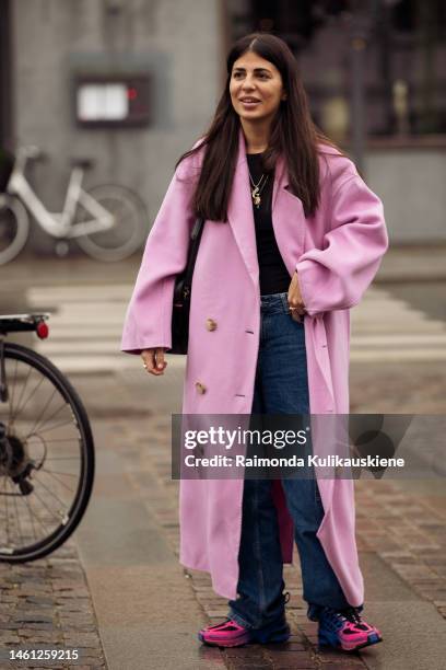 Guest wearing blue jeans, black top, pink long coat, and pink sneakers outside Latimmier during the Copenhagen Fashion Week Autumn/Winter 2023 on...