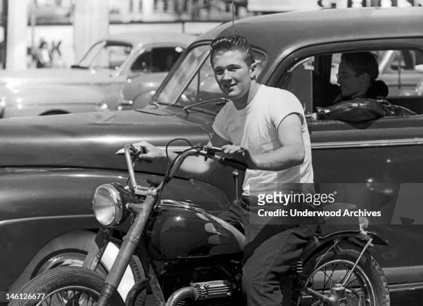 Young man on a motorcycle next to his buddy wearing a leather jacket in a car, San Francisco, California, mid 1950s.