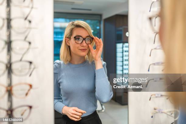 cliente rubia caucásica mirando su reflejo en el espejo - miopía fotografías e imágenes de stock