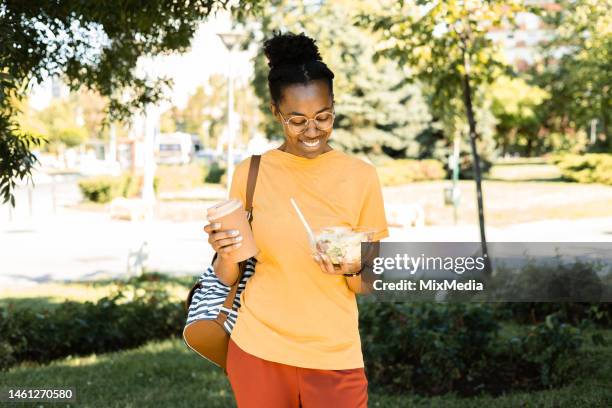 happy african girl enjoying her lunch break with coffee and salad - eating on the move stock pictures, royalty-free photos & images