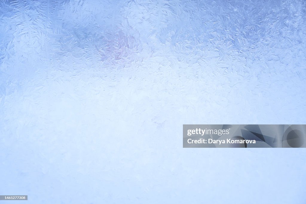 Beautiful frosty pattern on the glass in the window. Blue background with copy space.
