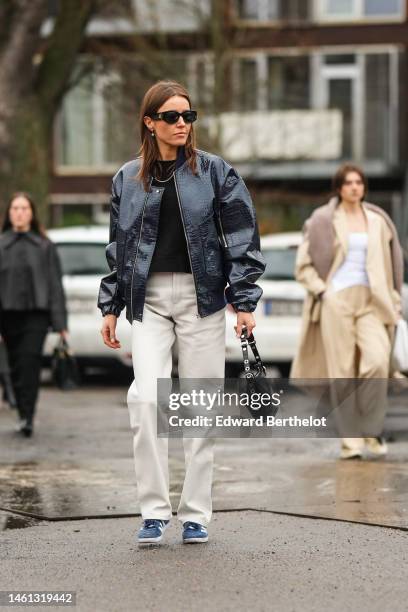 Guest wears black sunglasses, gold ring, silver earrings, a navy blue shiny varnished leather crocodile print pattern bomber coat, a black shiny...