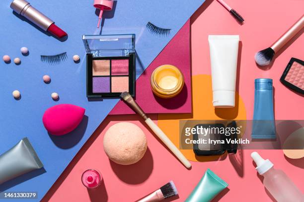 set of beauty products laid out on a multi-color background. cosmetic make-up  products for a woman make-up brush, red lipstick, false eyelashes, face powder blush palette, eyeshadow, face cream hand cream, beauty blender sponges, face serum and lip balm. - makeup stock-fotos und bilder