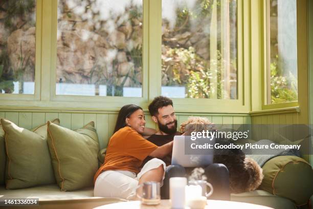 smiling couple petting their dog while using a laptop on their sofa - ungt par bildbanksfoton och bilder