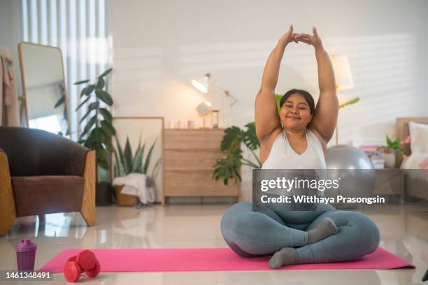 asian overweight woman exercising yoga seated side bend pose alone on the floor in house - fat asian woman stock-fotos und bilder