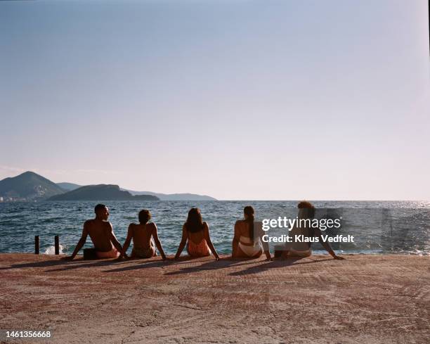 young friends admiring sea while sitting on pier - budva stock pictures, royalty-free photos & images