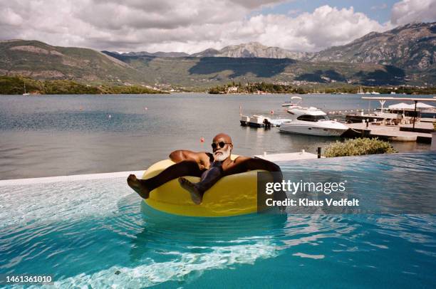 senior man with sunglasses floating on inflatable ring - completely bald stock photos et images de collection