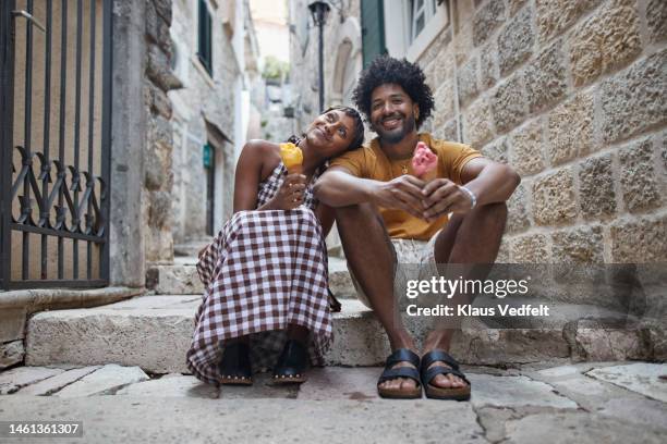 man sitting on steps with girlfriend holding ice cream - freundinnen urlaub sommer eis stock-fotos und bilder