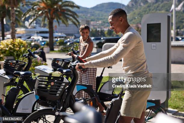 young man taking out electric bicycle by friend at station - bicycle parking station stock pictures, royalty-free photos & images