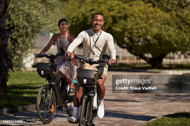 man riding electric bicycle with girlfriend in park - bicycle rental stock-fotos und bilder