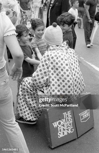 View, from behind, of a clown sitting and talking with three children on 9th Avenue in Hell's Kitchen during the International Food Festival, New...