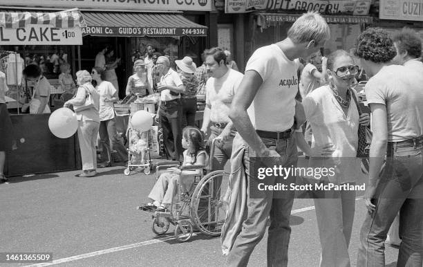 Man pushes a young girl in a wheelchair on 9th Avenue in Hell's Kitchen during the International Food Festival, New York, New York, May 20, 1978.