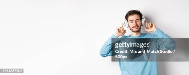 relaxed young man enjoying favorite song,listening music in - young men white background stock pictures, royalty-free photos & images