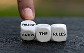 Hand turns dice and changes the expression 'know the rules'. to 'follow the rules'.