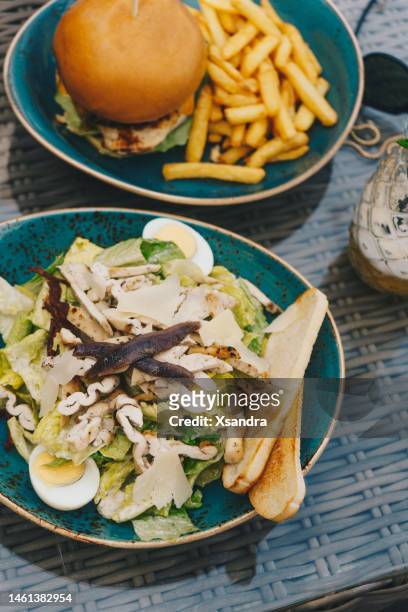 caesar salad and burger with fries served on the outdoor terrace - anchovy stock pictures, royalty-free photos & images