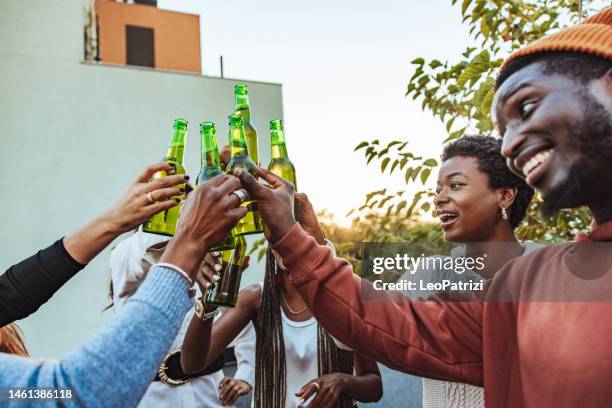 group of young friends toasting with beer at a party - reünie sociaal stockfoto's en -beelden