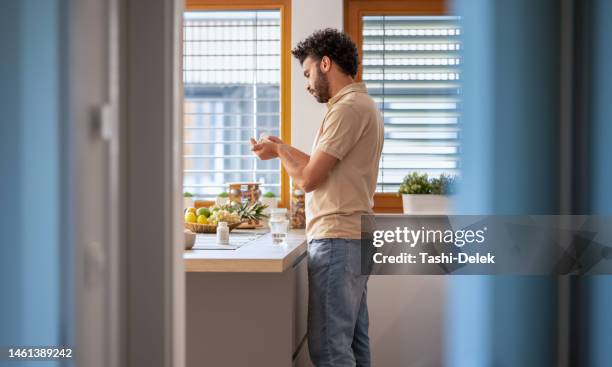 young man taking medicine with water at home - man glasses tablet in kitchen stock pictures, royalty-free photos & images