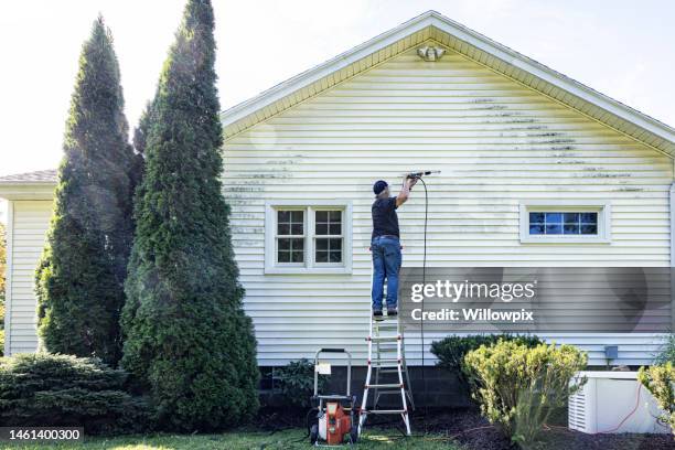 homem sênior up on ladder diy power washing house siding - high pressure cleaning - fotografias e filmes do acervo