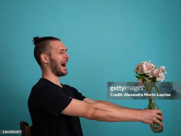 white man terrified by holding flowers on a turquoise background - unrequited love stock pictures, royalty-free photos & images
